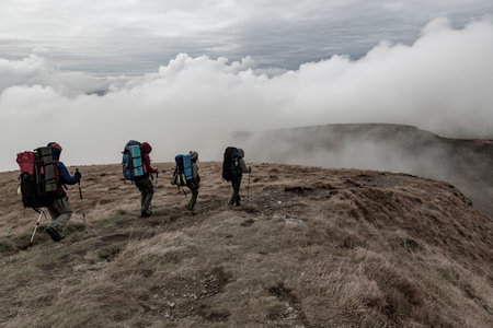 Group of hikers on the mountain range with strong wind and low clouds. Rainy weather, mute colorsの写真素材