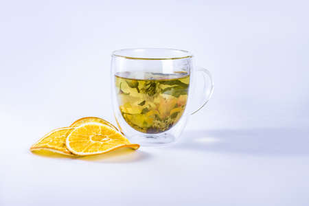Flower tea in the double wall glass cup and next to it lie dried pieces of orange.の写真素材