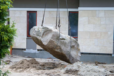 Very heavy stone is picked up and tied with steel straps. Safe handling of a very heavy granite boulder with a crane.の写真素材