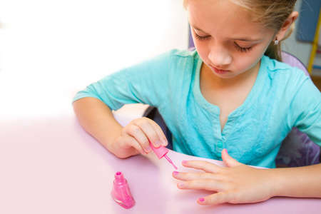 The girl in a turquoise T-shirt paints her nails with pink nail polish.の写真素材