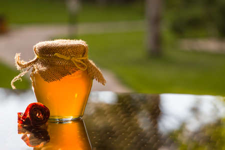 Jug of honey on the table in the garden. The sun shines through a glass jugの写真素材