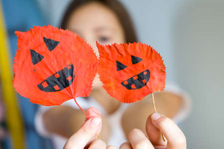 The child holds pictures of a pumpkin for Halloween on the leaves of a tree.の写真素材