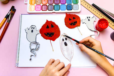 The child draws a ghost on a leaf of a tree. Preparing for the celebration of Halloween.の写真素材