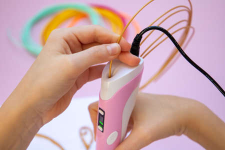 The child's hand inserts a plastic thread into a 3d printing pen.の写真素材