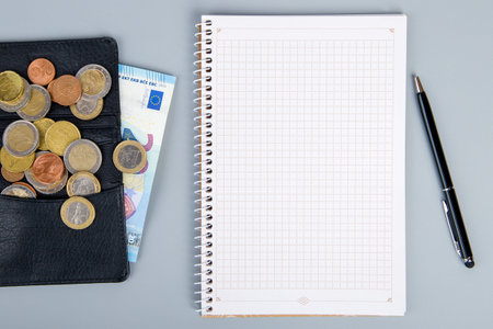 Open notebook with coins and a pen on a gray background. top viewの写真素材