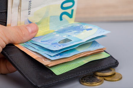 the hand holds euro banknotes and coins in the black wallet, close-upの写真素材