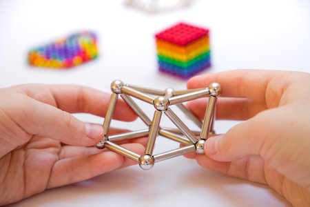 Child's hands assembling a pyramid of metal rods on a white background. Silver constructor made of magnetic sticks and ballsの写真素材