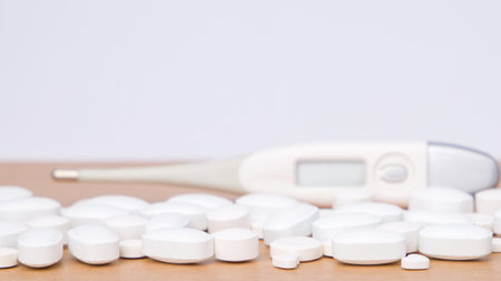 Pills and thermometer on white background. Focus on foreground.