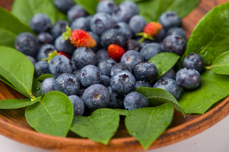 Fresh blueberries in a wooden bowl with green leavesの写真素材
