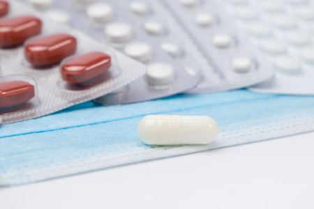 Pills and medical mask on white background. Selective focus.