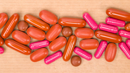 close up of red and pink pills on a wooden background with copy space