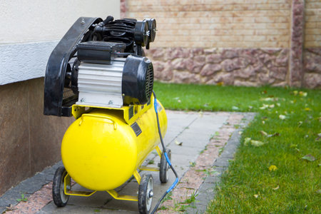 Yellow air compressor on the background of the lawn and the wall of the house.の写真素材