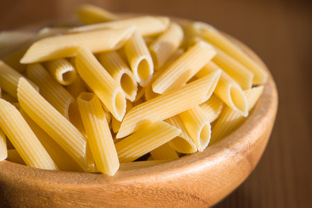 close up of penne pasta in a wooden bowl on wooden table, selective focusの写真素材