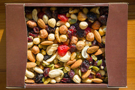 Mix of nuts and dried fruits in a box on wooden background. Top view.