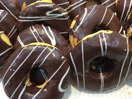 Display of delicious pastries in a bakery with assorted glazed donuts on trays in a shop counterの写真素材