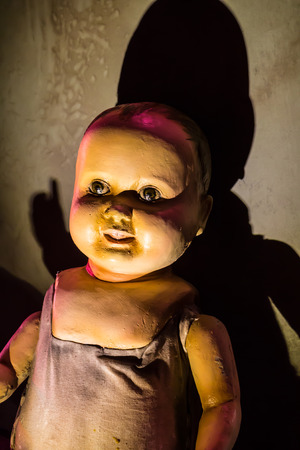 A scary old, broken doll against a damaged wall.の写真素材