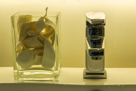 Faucet and seashell vase on ceramic sink.