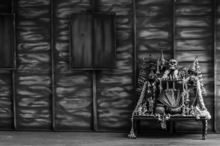 black and white Halloween still life Thai theme: Scary decorated dark room with witch altar table covered in spider webs,
skull, candlestick, devil doll and old wood wall background.の写真素材