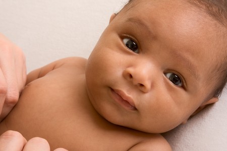 Thoughtful biracial mix of Hispanic and African American infant lying down on yellowish colored blanketの写真素材