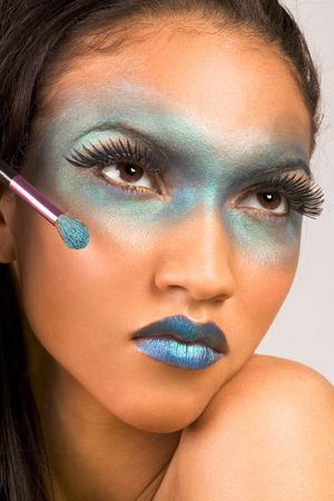 Young female beauty fashion model of mixed Creole and African-American ethnicity covered in dramatic blue make-up and holding makeup brushの写真素材