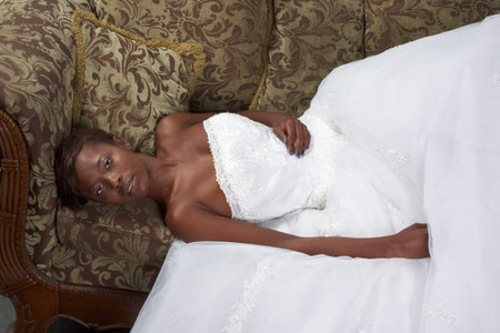 African American happy female in white gorgeous wedding gown lying down on couchの写真素材