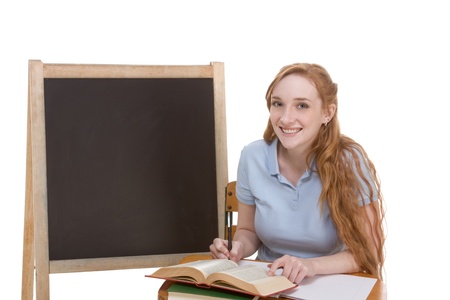 High school or college Caucasian redhead woman student sitting by the desk. Blank blackboard with copyspace is visible in backgroundの写真素材