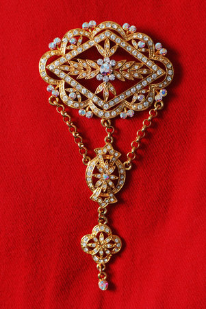 Gold brooch with many diamonds and gems, on red cloth backgroundの写真素材