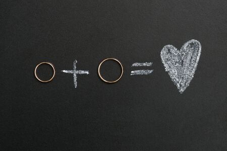 Wedding rings and plus and heart drawing with calk on calkboard. Husband and wife or groom and bride, married couple concept.の写真素材