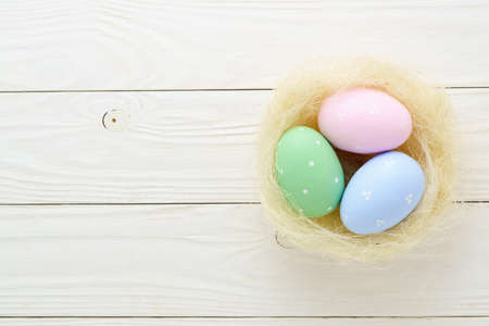 Easter nest with painted colorful eggs on white wooden background. Top view with copy space.の写真素材