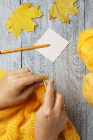 Woman knitting a warm wool sweater on knitting needles with yellow yarn. Close-up view with female hands.の写真素材
