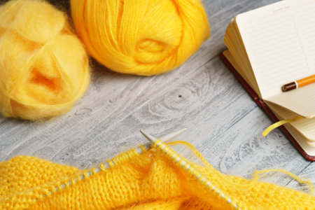 Wool yarn, knitting needles with knitted wool fabric, notebook and pencil on a rustic wood table. Handicraft work. Handmade, knitting hobby.の写真素材