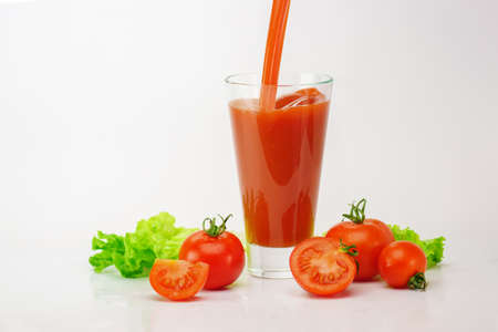 Glass of tomato fresh juice with raw tomatoes and salat leaves on light background.の写真素材