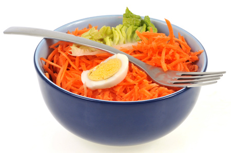 Bowl of grated carrots with a boiled egg and a salad leafの写真素材