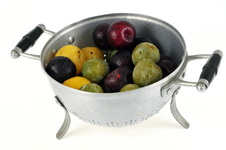 Plums of different colors in a colander on a white backgroundの写真素材