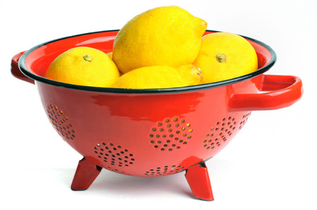 Yellow lemons in a red colander on a white backgroundの写真素材