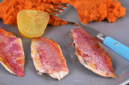 Red mullet fillets in a plate with a slice of lemon and mashed carrots close-up