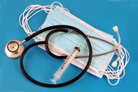 Stethoscope with masks and syringe close-up on blue backgroundの写真素材