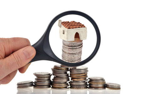 Real estate investment concept with a magnifying glass and a house on a pile of coins close up on a white backgroundの写真素材