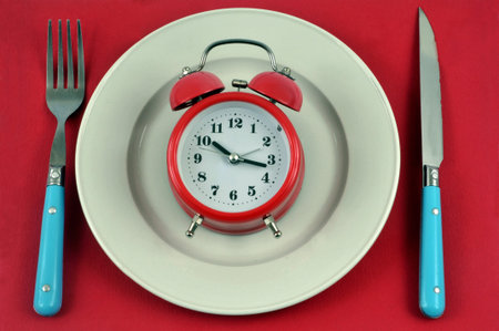 Mealtime concept with an alarm clock in a plate surrounded by cutlery