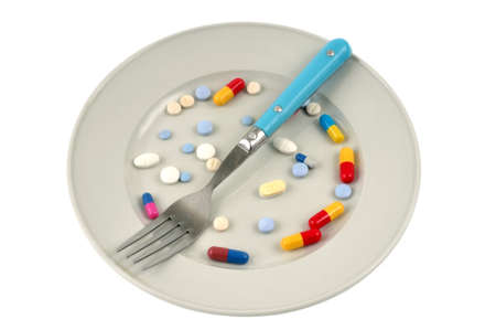 Food and vitamin supplements in a plate with a fork on a white backgroundの写真素材
