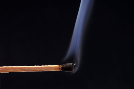 Extinguished matchstick with smoke close-up on black background