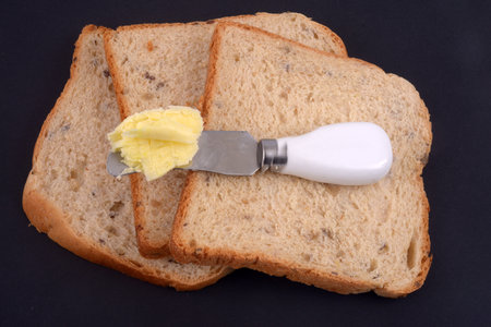 Knife with butter lying on slices of sandwich bread on black backgroundの写真素材