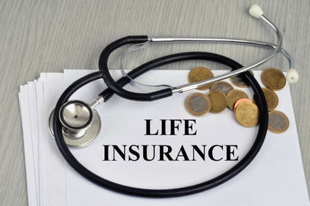 Life insurance concept with a stethoscope and cash money lying on a contract in Englishの写真素材