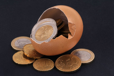 Eggshell filled and surrounded by euro coins close-up on black background