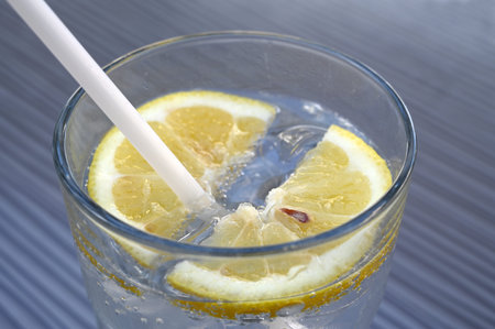 Glass of sparkling water with a slice of lemon and a straw close-up
