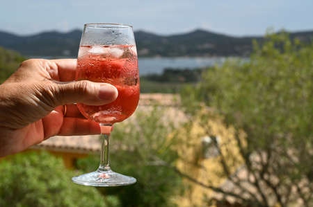 A glass of wine with ice cubes in handの写真素材