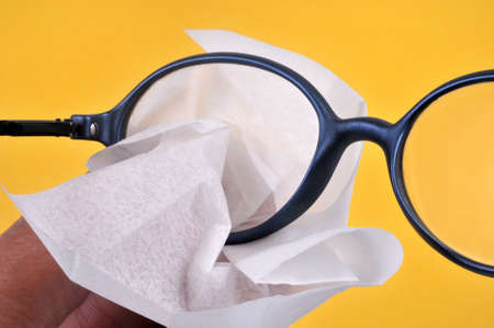 Clean his glasses with a wipe close-up on yellow backgroundの写真素材