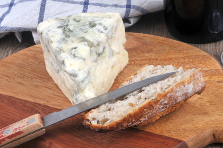 Piece of French blue cheese on a cutting board with a knife and pieces of bread close-up