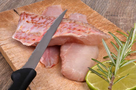 Knife on raw red mullet fillets laid on a cutting board with a slice of lemon and rosemary close-upの写真素材