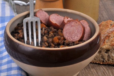 Dish of lentils with slices of smoked sausage served in a bowl with a fork close upの写真素材